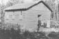 P2008.107.2: Mr. and Mrs. McTavish standing outside the first schoolhouse in McMurray, circa 1912