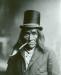Elderly man with pipe in mouth top hat on with long hair