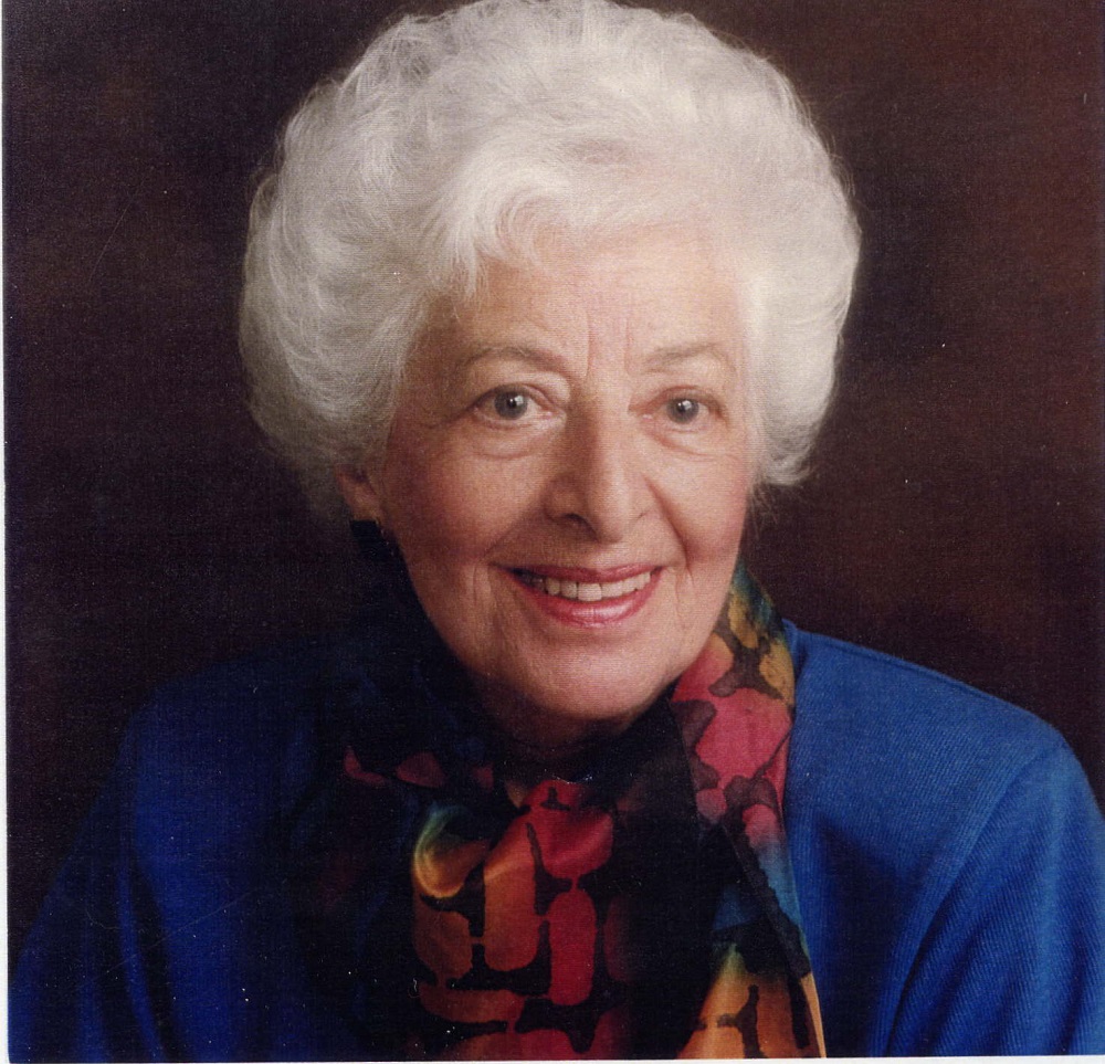Formal portrait of woman with white hair and blue jacket with multi-coloured scarf