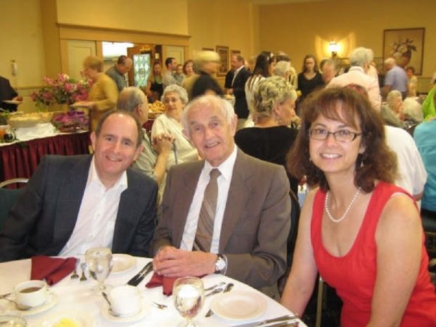 Two men and a woman seated at a dining table - others can be seen in the background