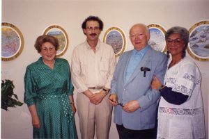 Two men and two women standing together – paintings on wall in background
