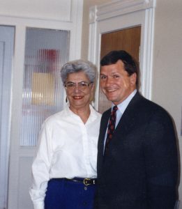 Une femme aux cheveux gris portant un chemisier blanc et un homme portant un complet sombre posant en souriant pour la photo.