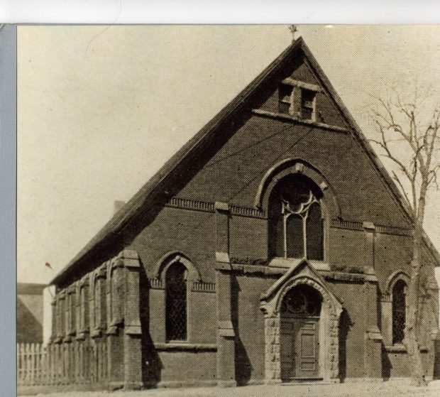 A stone building with a sharp peaked roof and door and windows with rounded arches over them