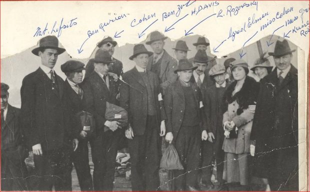 Group of 12 men and 2 women – men in suit jackets and hats or caps, women in overcoats and hats
