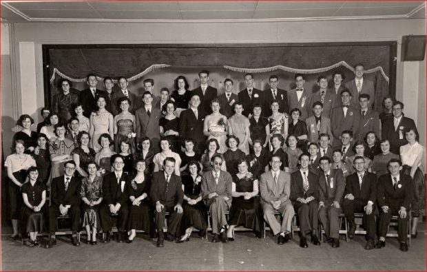 70 young men and women in business suits and in evening dresses arranged in four rows