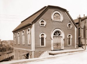 Immeuble en bois comportant une porte centrale et cinq fenêtres surmontées d’arcs arrondis.