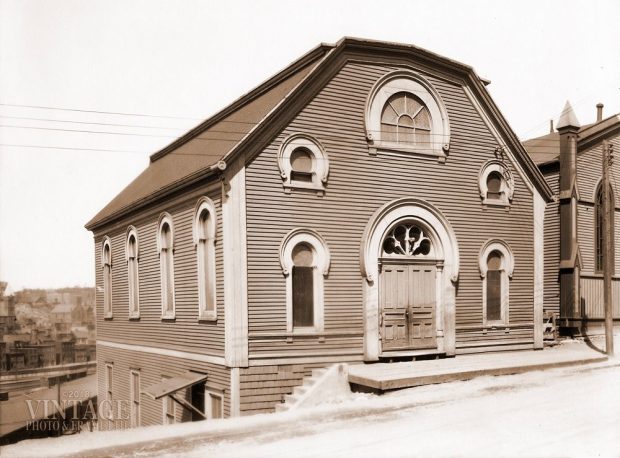 A wooden building with a central door and five windows with rounded arches over them.