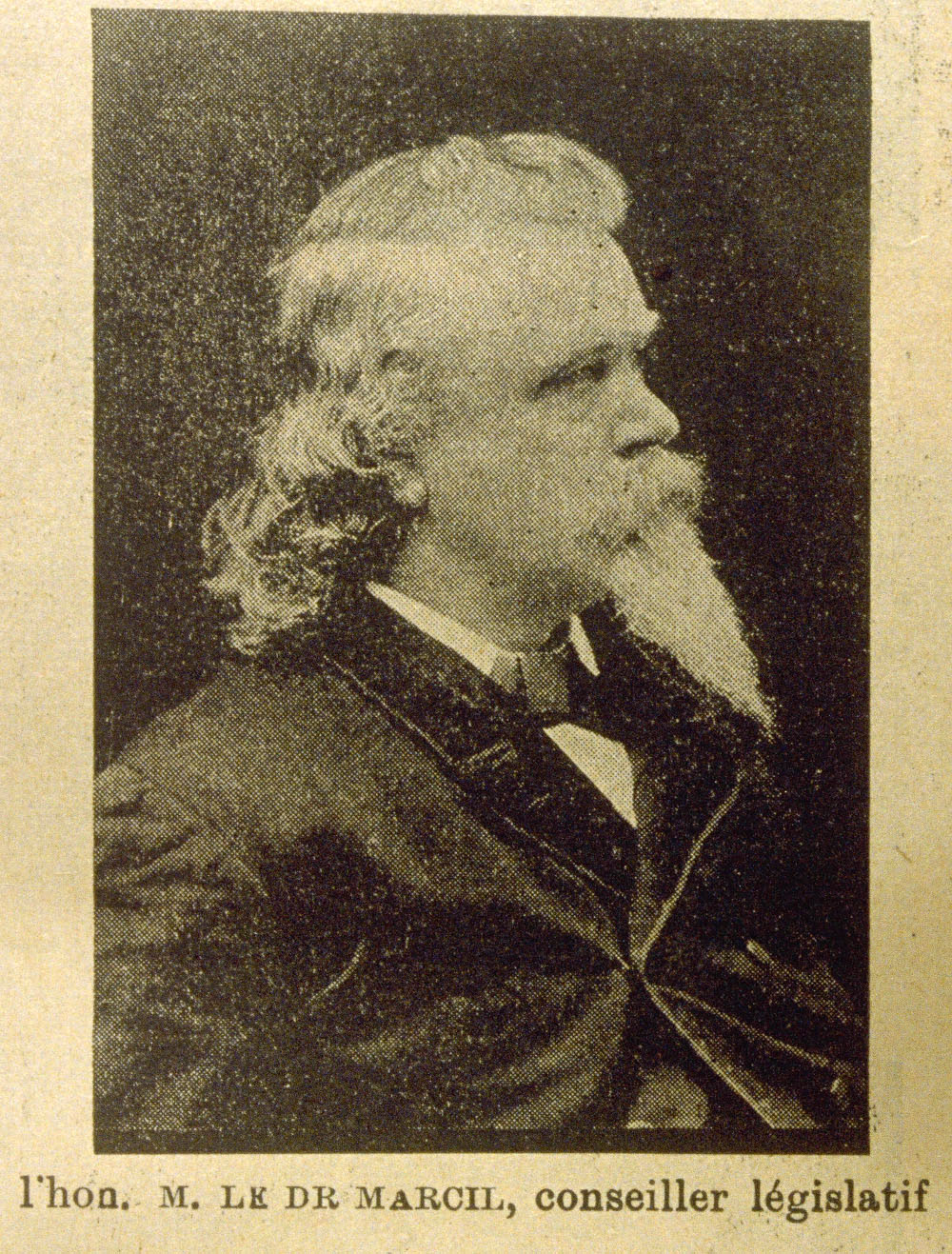 Black and white photograph of a man in profile wearing an elegant black jacket. His curly hair hangs down past his neck, and his mouth and chin are covered by an enormous moustache and a long goatee.