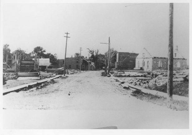 Black and white photograph of a street that has been completely devastated by fire. Houses, businesses and other buildings have been seriously damaged.