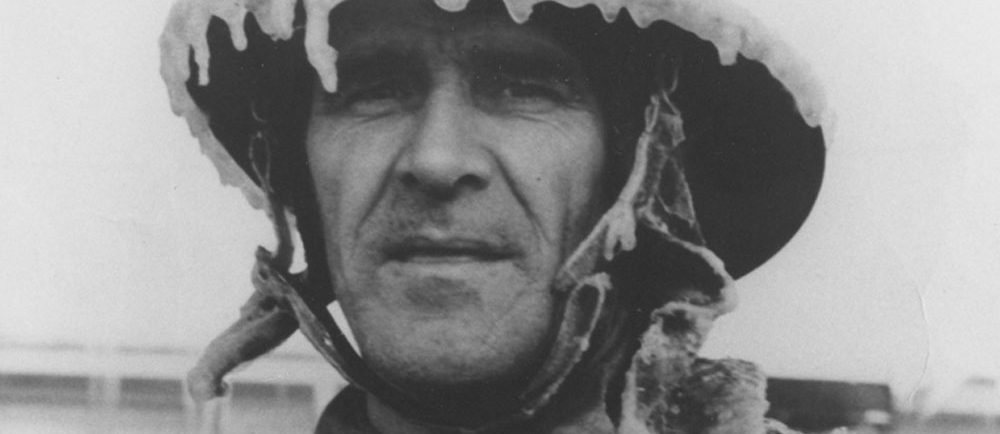 Black and white photograph of a peaceful-faced man wearing ice-covered firefighter’s gear.