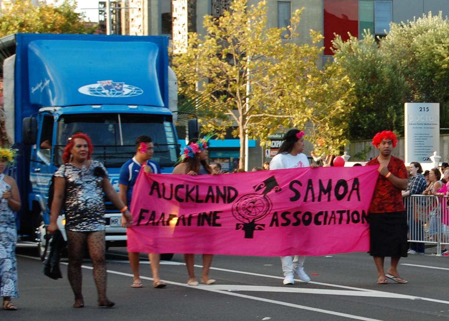 Five people holding a banner in a street parade. The banner reads AUCKLAND SAMOA FAAFAFINE ASSOCIATION.