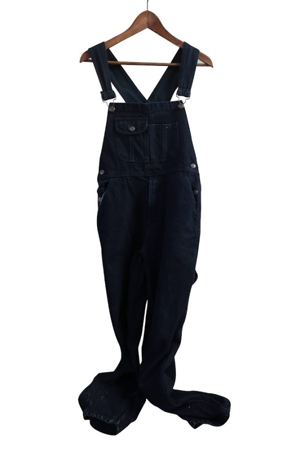 Black overalls on a wooden hanger.