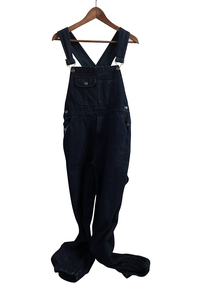 Black overalls on a wooden hanger.