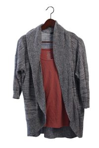 Grey cardigan over a pink shirt, on a wooden hanger.