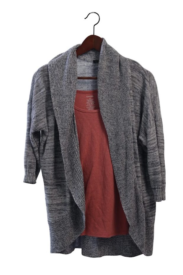 Grey cardigan over a pink shirt, on a wooden hanger.