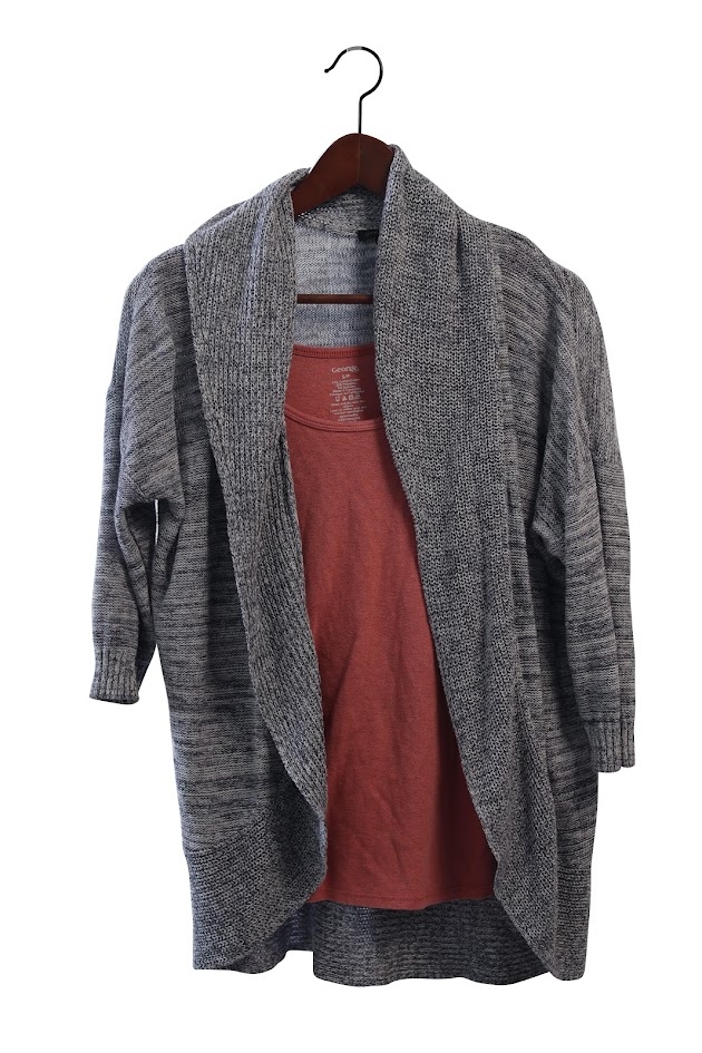 Grey cardigan over a pink shirt, on a wooden hanger.