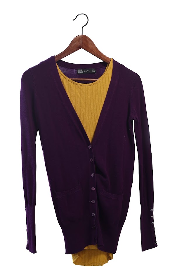 A purple cardigan buttoned up over a yellow shirt, on a wooden hanger.