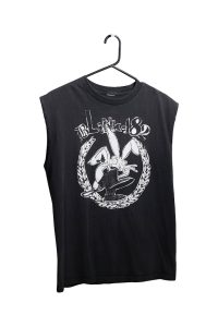 A black tank top hanging on a black hanger. There is a white text on the front reading Blink-182. Below the text is graphic of a laurel wreath framing a cartoon rabbit wearing black boots.