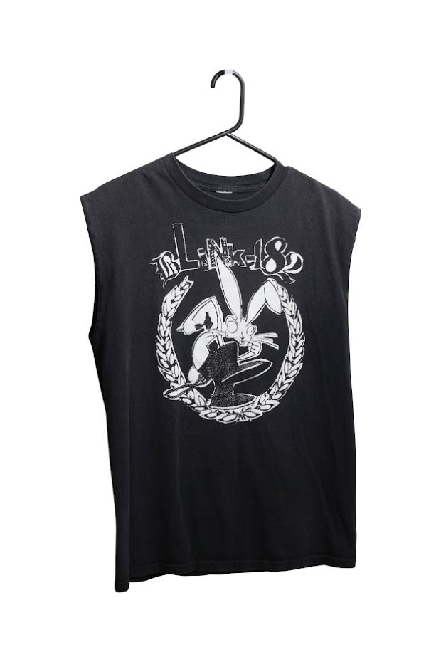 A black tank top hanging on a black hanger. There is a white text on the front reading Blink-182. Below the text is graphic of a laurel wreath framing a cartoon rabbit wearing black boots.