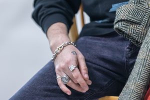 A hand with rings and a silver chain bracelet resting on a leg clad in purple denim.