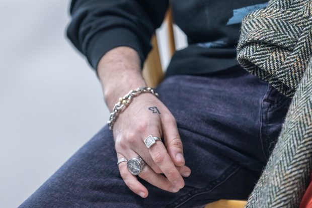 A hand with rings and a silver chain bracelet resting on a leg clad in purple denim.