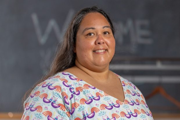 Portrait photo taken from mid-chest up. The person is smiling and looking into the camera. She is wearing a white v-neck shirt with a purple, blue, and orange pattern of stylized birds.