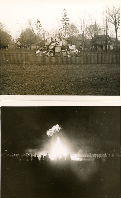 Two black and white photographs of a bonfire in a park setting; top image taken during the day depicts a large pile of wooden items surrounded by a temporary snow fence; bottom photo take at night depicts a lit bonfire with numerous people gathered around