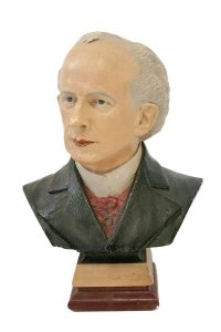 A coloured plaster bust of a man with receding grey hair wearing a white shirt, red cravat and black jacket