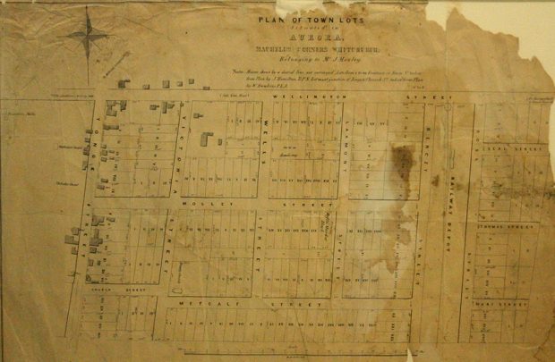 An old creased, stained and torn map of building lots in Aurora laid out on a grid depicting lot numbers and street names