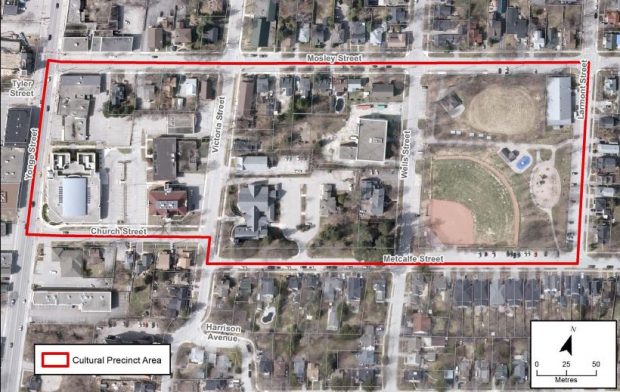 A colour aerial photograph of three blocks in Aurora known as the Cultural Precinct outlined in red; streets are labelled and directional and distance scales included in lower right corner