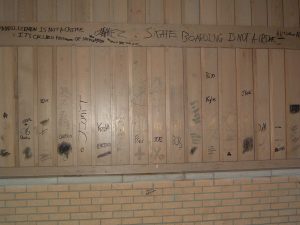 A photograph of a wooden and brick wall with graffiti written across in black ink