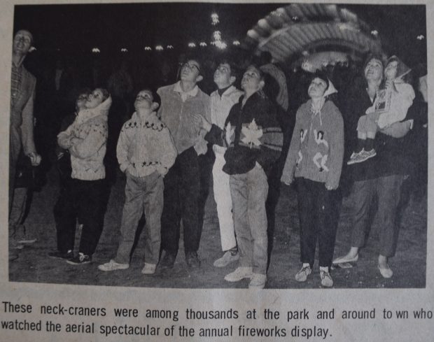 A black and white newspaper clipping showing a photograph of a group of people looking up into the night sky; lighted stage in background; typed text underneath