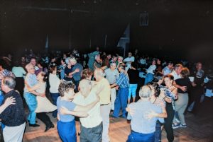 Colour photograph of a dance party underway in Montmagny during the Carrefour mondial de l’accordéon. Dozens of smiling dancers move to the sounds of the accordion.