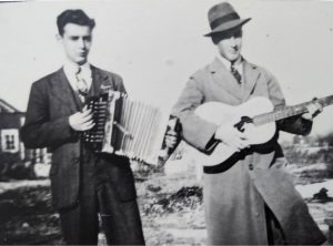 Black and white photograph of Armand Labrecque. He is on the right, holding an accordion. The shot was taken at a family gathering, with Mr. Casault standing next to him with a guitar.