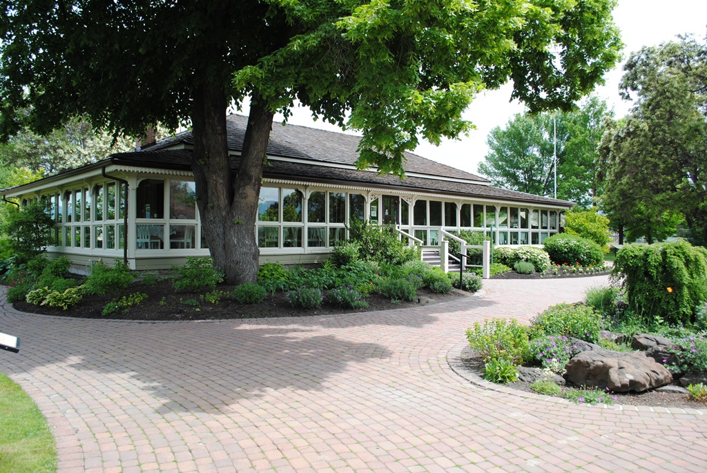 Colour photo of a one-storey building with a large, wraparound enclosed porch. Curving walkways surround the building.