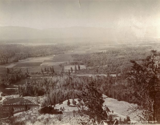 Black and white photo with expansive view from the top of a hill looking across the valley with its fields and treed areas.