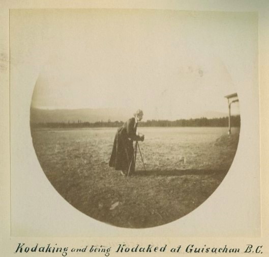 Black and white round photo of a woman in a field with an old-fashioned camera on a tripod.