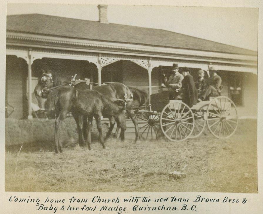 Black and white photo of a horse and wagon with four people in front of a house.