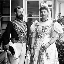 Black and white close up photo of a man and woman in formal clothes posing in front of a window.