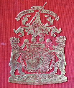 Silver family crest on a red background of two lions flanking shields with the motto 