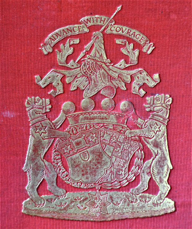 Silver family crest on a red background of two lions flanking shields with the motto Advance With Courage above.