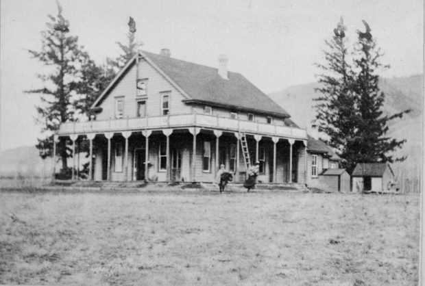 Black and white photo of the front and side of a two-storey house with a wrap-around verandah and balcony. There are two children standing in front of the house.