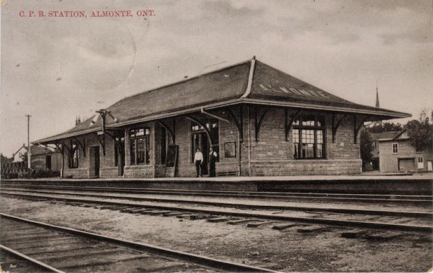 Black and white photographic postcard of the Almonte train station taken across the tracks, 1950s