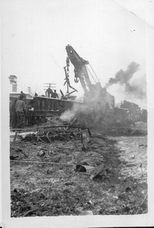 Photograph of the clean-up process in the aftermath of the train wreck in Almonte, 1942. There is a crane in the background, and men standing in the wreckage.