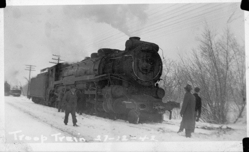 Photographie du train militaire après l’accident ferroviaire d’Almonte plus loin sur la voie ferrée, à distance d’Almonte; on y voit des hommes debout dans la neige autour de la locomotive, 1942