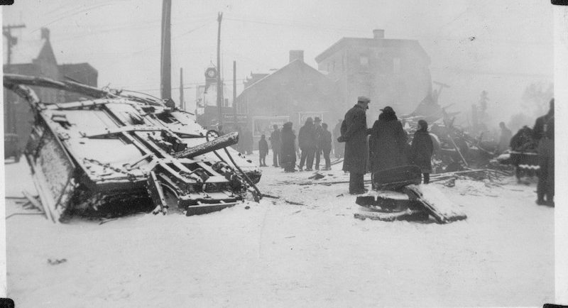 Photograph of the wrecked third coach of the Ottawa Valley Local in Almonte with people walking through town, 1942