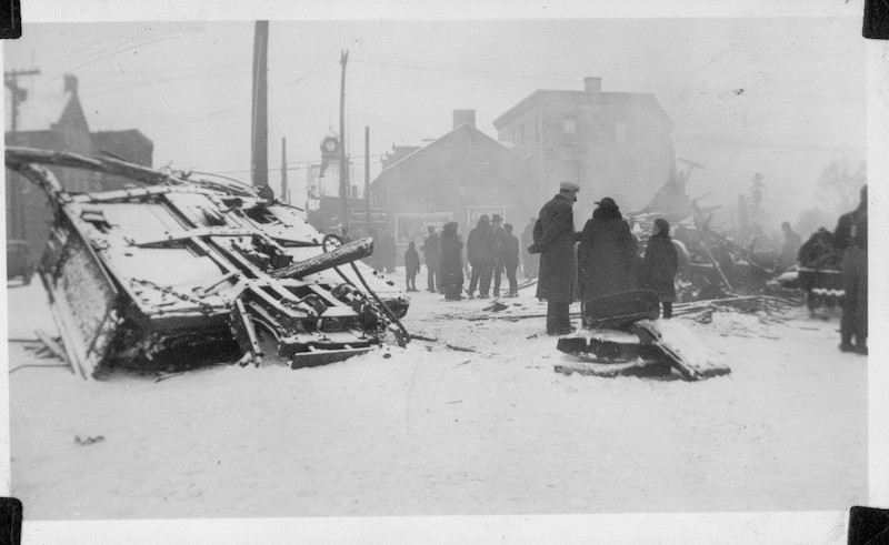 Photograph of the wrecked third coach of the Ottawa Valley Local in Almonte with people walking through town, 1942