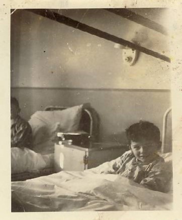 Photograph of a small boy , Bernard Turcotte in a hospital cot, sitting up and smiling for the camera at the Ottawa Civic Hospital after the Almonte Train Wreck, 1943