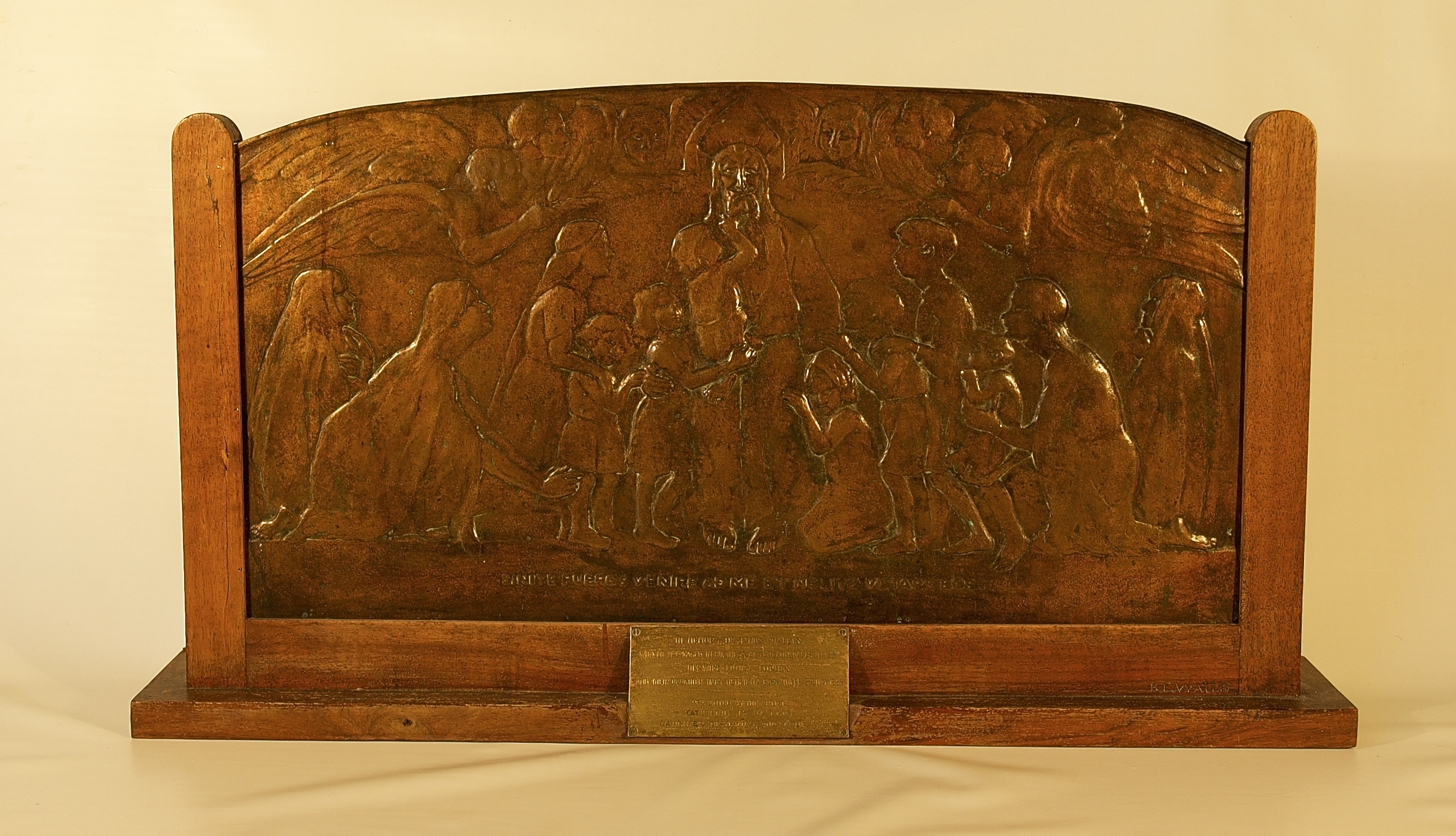 A bass engraved plaque showing Jesus surrounded by children and flanked by two angels.