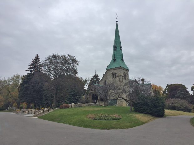 A photograph of St. James 'the Less' Anglican Church in Toronto, Ontario. The stone church has a large bronze steeple that has aged green.